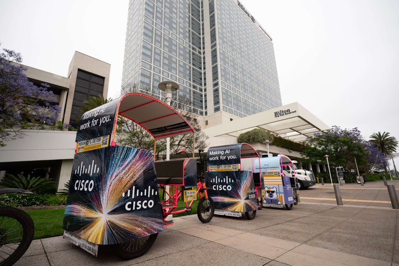 Xion electric pedicabs with sponsor wraps lined up on a city street